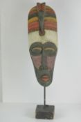 A carved and painted wooden African mask on stand, 80cm high.
