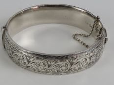 A HM silver hinged bangle having floral engraved decoration to front, with safety chain,