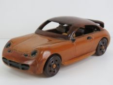 A lacquered wooden model of a two door car, 25cm in length.