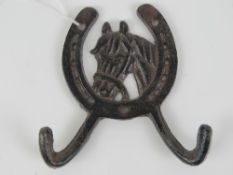 A double coat hook having horse head and horseshoe to centre, 12cm wide.