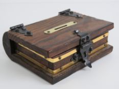 A wooden money box in the form of a book, having brass escutcheon and black metal hinges. 18 x 15cm.