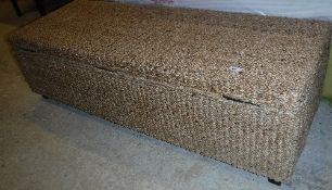 A modern seagrass covered ottoman on stained wood square tapered legs,