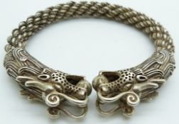 A Chinese white metal bangle depicting dragons and rope twist decoration