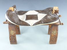 An Eastern camel seat or stool with brass studded decoration to the legs and leather cushion, 60cm