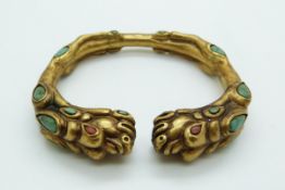 A brass gilt bangle set with turquoise and coral sections in the form of a dragon