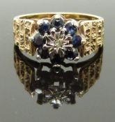 A 9ct gold ring set with a diamond and sapphires with textured shoulders, size O/P, 4.80g