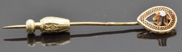 A stick pin set with a diamond within a filigree border
