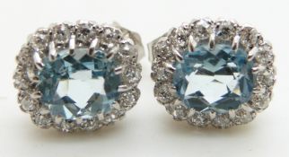 A pair of 9ct white gold earrings each set with an oval cut aquamarine surrounded by diamonds