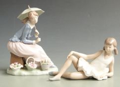 Two Nao figurines, one holding a parasol with baskets of flowers, the other a reclining ballerina,