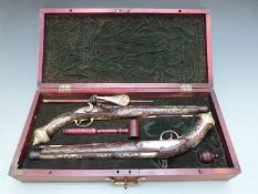 A pair of flintlock action duelling pistols with carved woodwork, brass and silver inlaid
