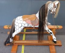A wooden dapple grey rocking horse with hair mane and tail, leather saddle and reins, metal mounts