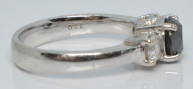 An 18ct white gold ring set with a round cut black diamond flanked by two diamonds, each