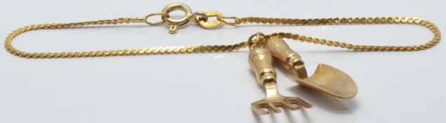 A 9ct gold bracelet with two 9ct gold charms depicting a trowel and fork, 2.9g