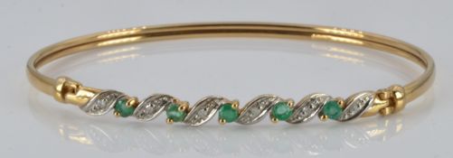 A 9ct gold bangle set with emeralds and diamonds, 4.9g