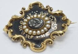 A Victorian enamel mourning brooch set with a flower plaque, black enamel and seed pearls reading '