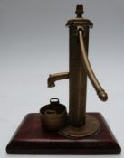 Brass Sanders patent miniature novelty village water pump with bucket below, on wooden base,