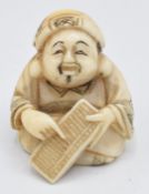 An early 20thC Japanese ivory netsuke depicting a man using an abacus, 3cm