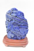 Chinese lapis lazuli carving of a mountainous scene on wooden stand, 18 x 12cm