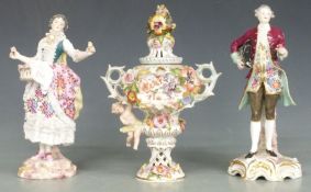 A pair of Dresden lace figures and a covered pedestal vase with applied flower decoration,