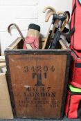 A wooden tea chest of walking sticks and umbrellas together with a woolen rug