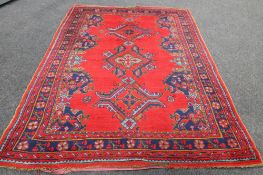 A Persian woollen rug of geometric design on red ground,