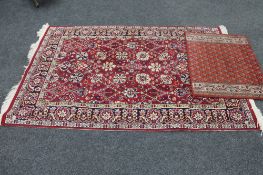 A fringed floral rug on red ground together with a further mat