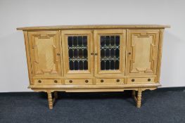 A blonde oak four door sideboard on raised legs