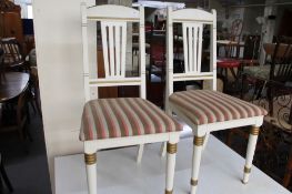 A pair of white and gilded dining room chairs.