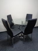A circular glass topped pedestal table and four black leather dining chairs on metal legs