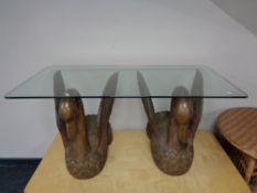 A rectangular glass topped coffee table on a pair of hardwood swan supports
