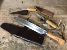 Three wooden handled hunting knives in leather sheaths.