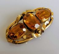 A Victorian three-stone citrine brooch on an elliptical gold frame with etched foliate decoration,