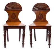 A pair of early 19th Century mahogany hall chairs: the backs with reeded lunette crestings and