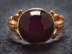 A cabochon garnet single-stone ring: in closed-back setting and between splayed shoulders,
