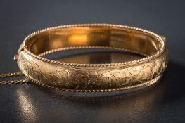 A 9ct gold hinged bangle: with attached safety chain, approximately 19gms gross weight,