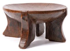 An Ethiopian carved wood stool: with oval dished seat on four swept legs, 29cm diameter.