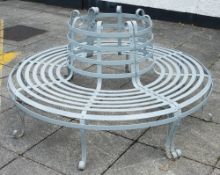 A wrought iron circular garden tree seat: in two sections of slatted design on scroll feet,