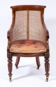 A William IV mahogany bergere armchair:, the curved cane panel back with paper scroll top rail,