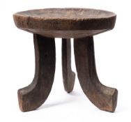 An Ethiopian carved wood stool: with oval dished seat on three curved legs, 37cm high.