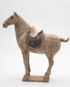 A Chinese pottery model of a horse: standing four-square, with grey painted saddle,