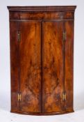 A George III mahogany bow-fronted hanging corner cupboard:, with a moulded cornice,