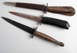 Two Fairbairn Sykes pattern knives: Third Pattern with cast ribbed grip, in brown leather scabbard,