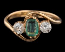 An emerald and diamond ring: the central rectangular cut emerald between two brilliant cut diamonds,