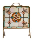 An Edwardian brass frame and stained glass firescreen:, with Art Nouveau scroll handle,
