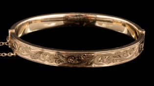 A 9 carat gold hinged bangle: half engraved with a foliate motif,