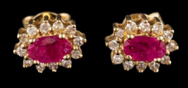 A pair of ruby and diamond earrings: the central oval cut ruby claw set within a surround of eight