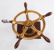 A small brass ship's helm: of five spokes with teak grips, mounted on a wooden plinth,