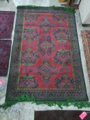 Machine made red ground rug with repeating motifs, in red, green, blue design and two small mats,