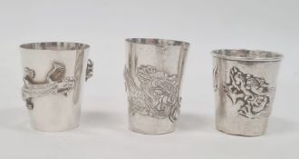 Three Chinese silver-coloured shot cups, each variously decorated with dragons or lizard and spider,
