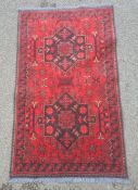 Modern Eastern-style red ground rug with two central medallions, in reds and blacks, 128cm x 76cm